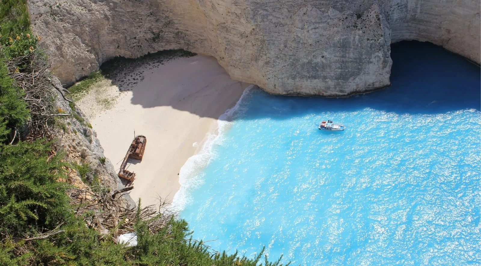 Navagio bay from above with an empty beach beside the wreck and a single small boat out on the water
