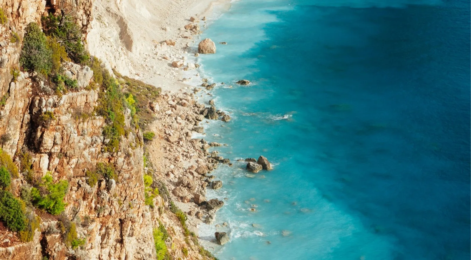 A steep limestone cliff shedding scree and boulders directly into turquoise water