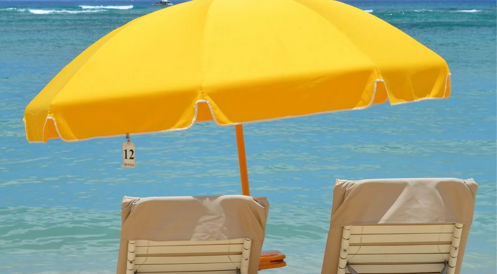 A hired yellow beach umbrella tagged number 12 with two empty loungers beneath it, facing flat turquoise water